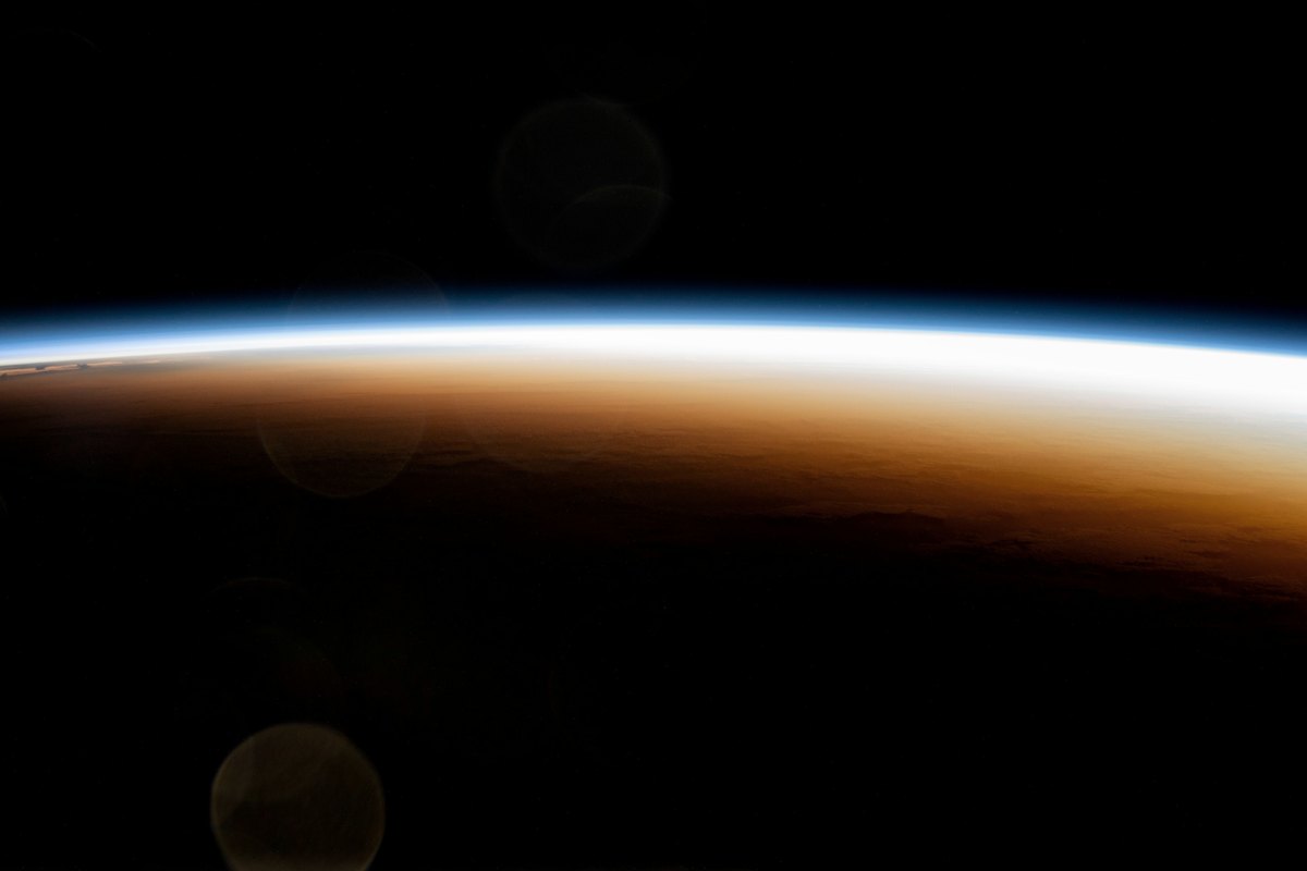 Curved amber and blue edge of Earth's atmosphere against black space, seen from orbit