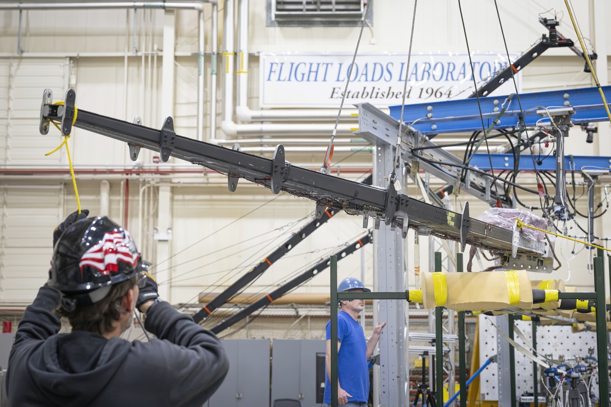 Technician in a hard hat, seen from behind, works on a long wing test structure in a laboratory