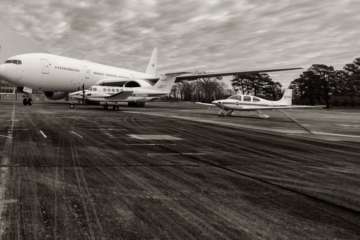 Black-and-white view of a jet and small aircraft parked on a cloudy-day ramp at Langley